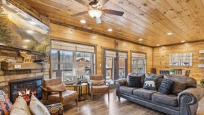 A cozy cabin interior with a fireplace, leather sofa, and wooden walls. - Eden Of The Smokies 5 Bedroom Cabin (Sevierville)