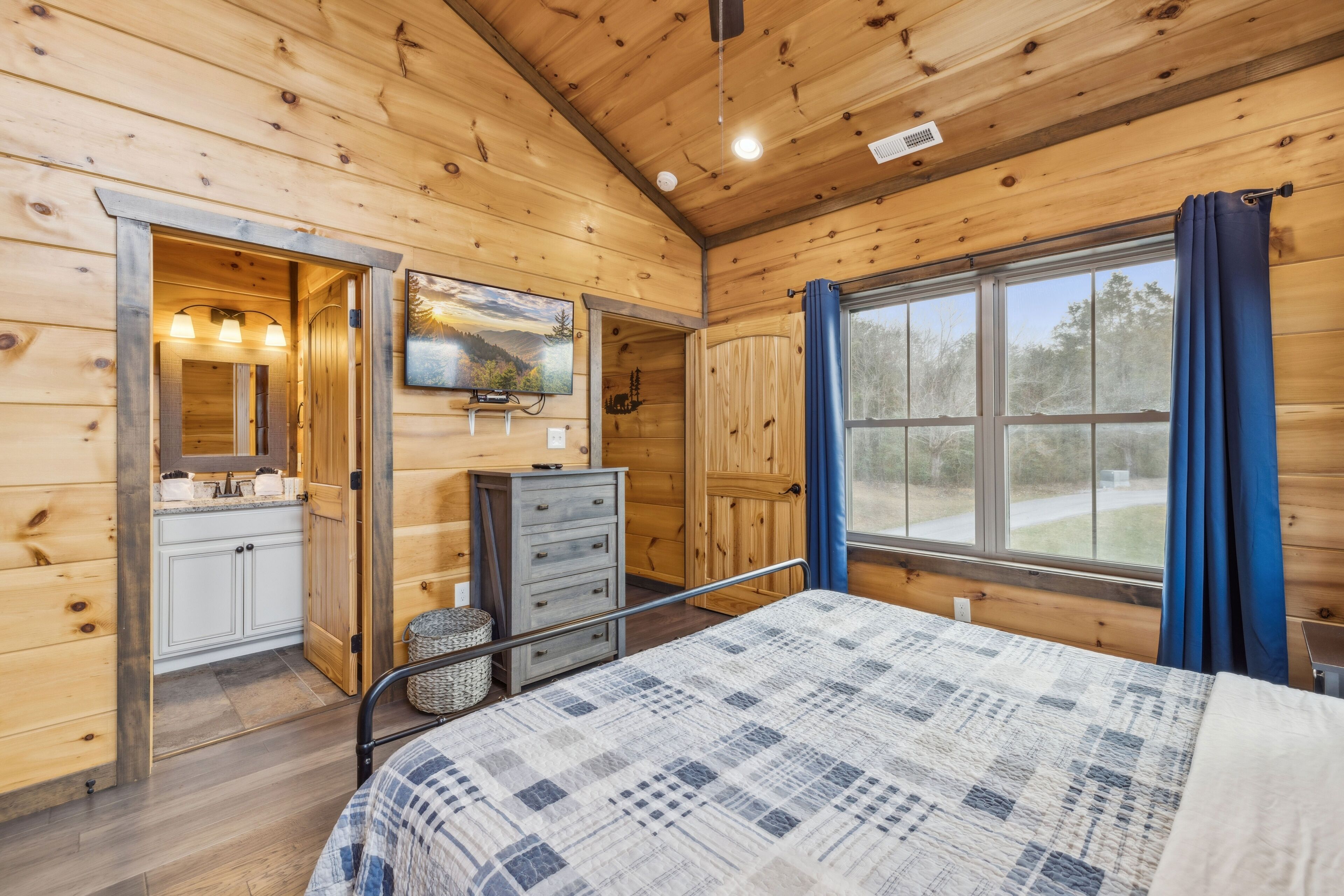Dormitorio de cabaña de madera con cama, cómoda y ventana con cortinas.