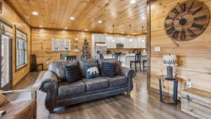 A cozy wooden interior with a leather sofa, a large wooden clock, and a kitchen area. - Eden Of The Smokies 5 Bedroom Cabin (Sevierville)