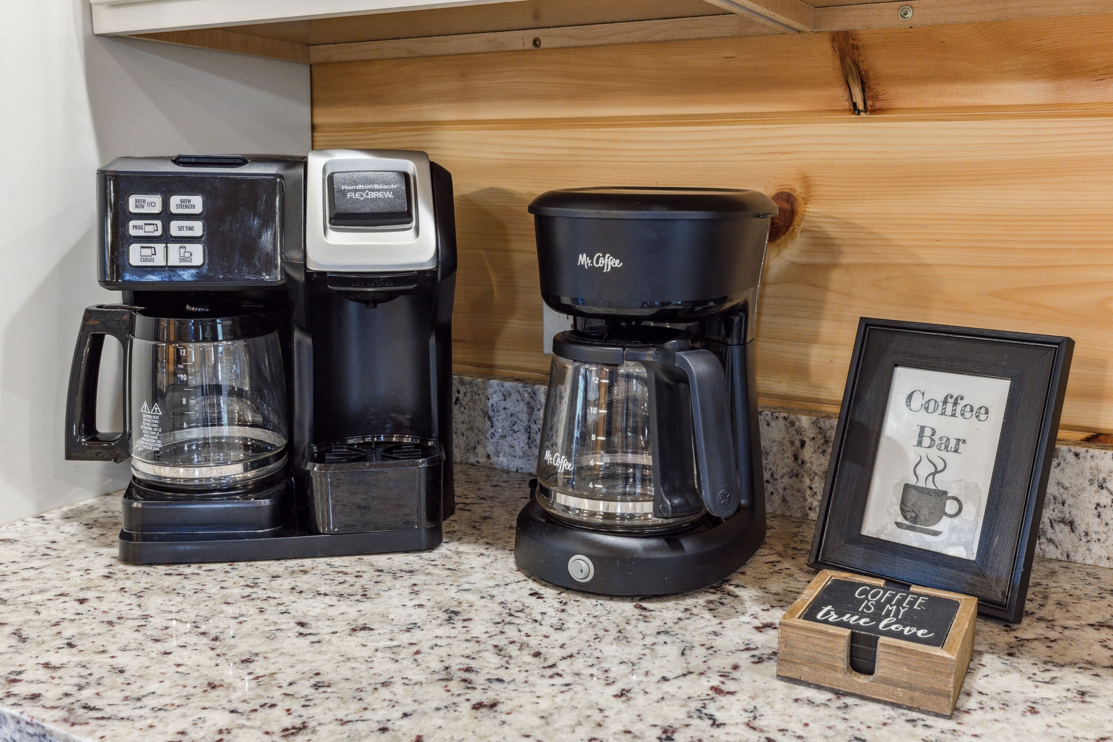 A coffee maker, a framed coffee cup sign, and a small wooden box with a coffee-themed message.