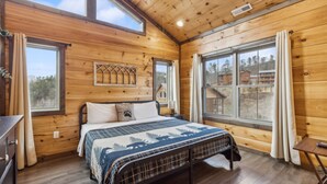 A wooden cabin bedroom with a bed, a nightstand, a window, and a view of the outside. - Eden Of The Smokies 5 Bedroom Cabin (Sevierville)