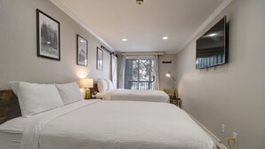 A hotel room with two beds, a flat-screen TV, a window with curtains, and framed pictures on the wall.
