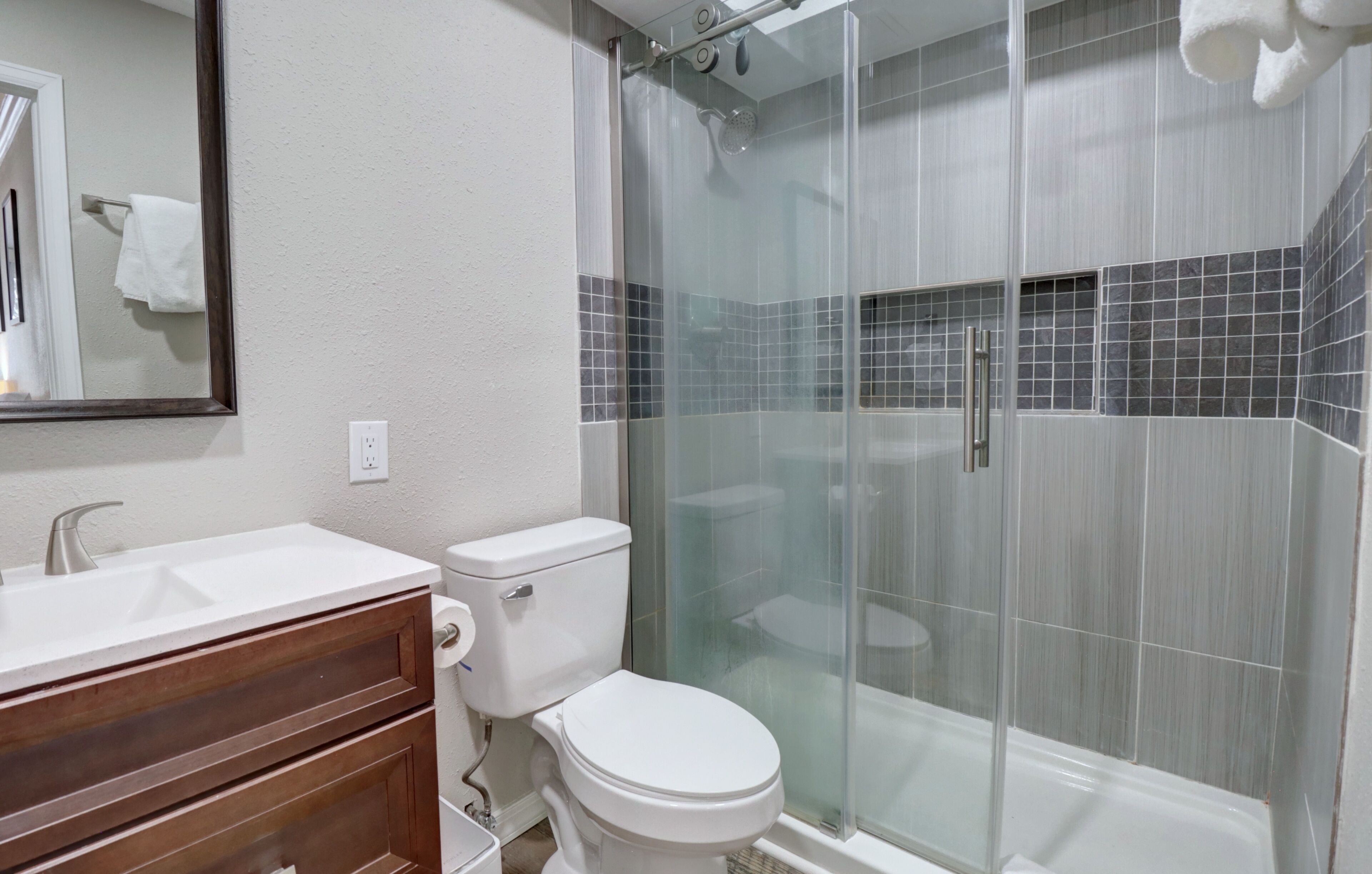A bathroom with a white sink, wooden vanity, toilet, and a glass-enclosed shower area.