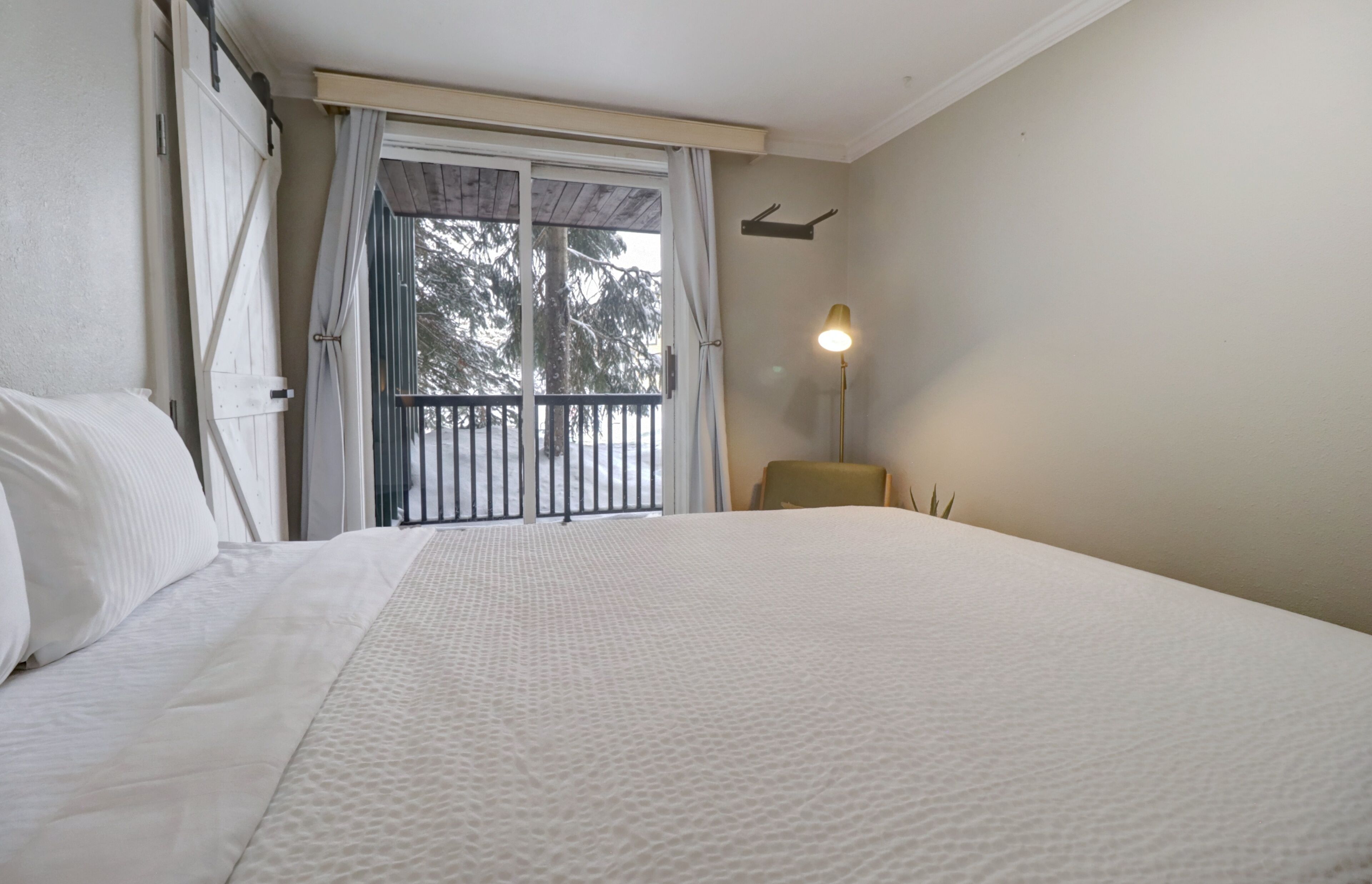 A hotel room with a large bed, a balcony with a view of trees, and a lamp on the nightstand.
