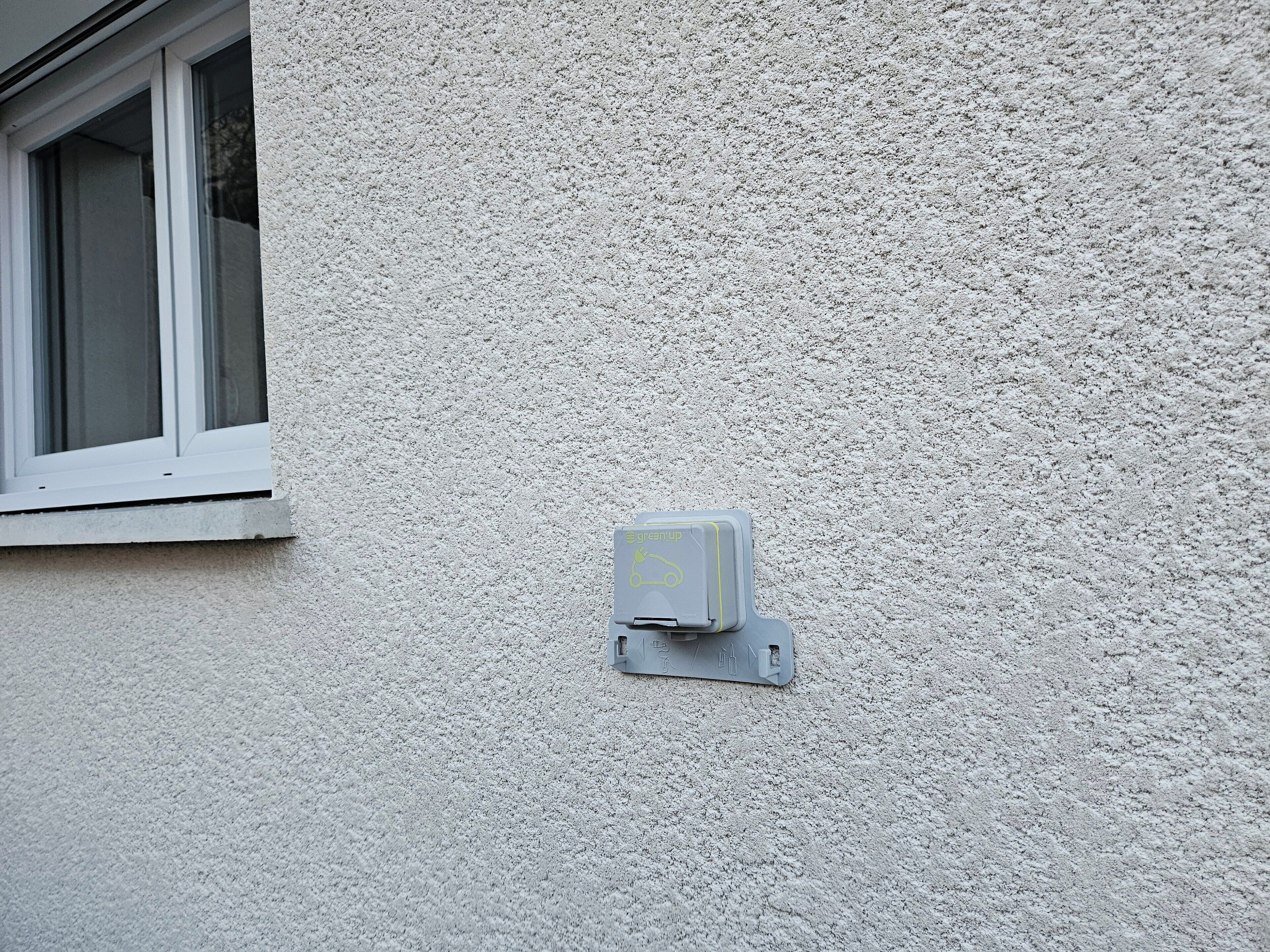 A utility box mounted on a textured wall near a window.