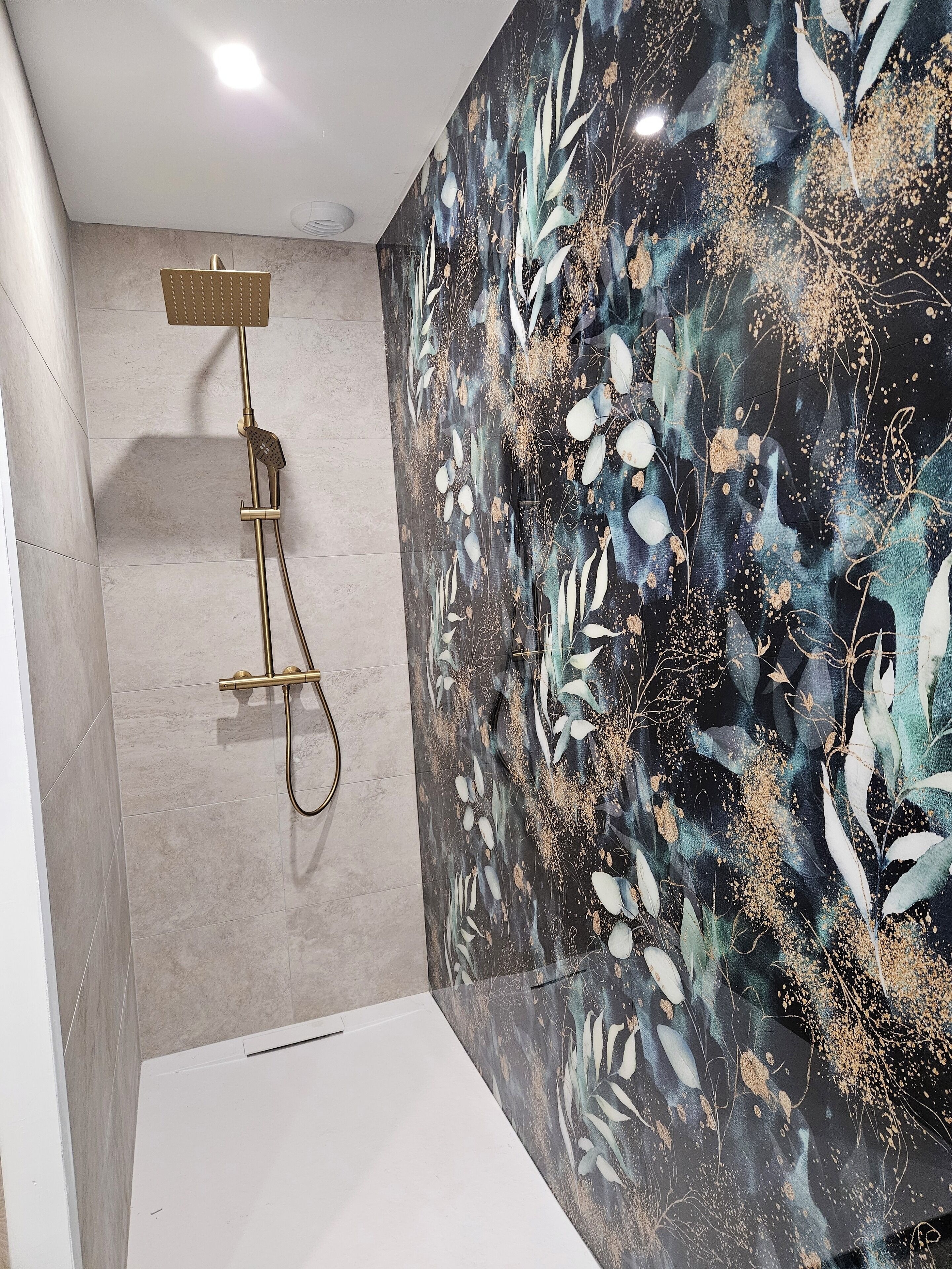 A modern bathroom with a shower, a large mirror, and a decorative wall.