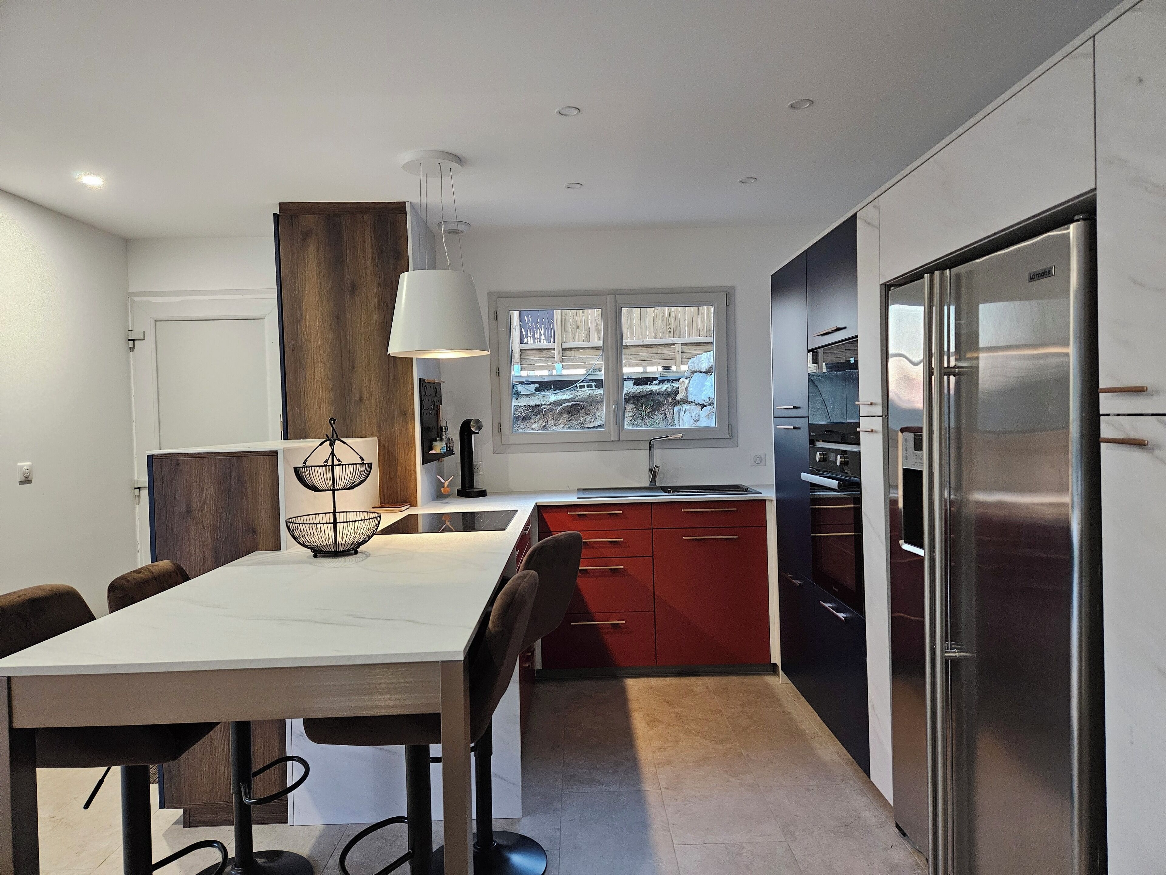 A modern kitchen with a dining area, featuring a large island, stainless steel appliances, and a view through the window.