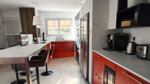 A modern kitchen with red cabinets, stainless steel appliances, and a bar area with stools. - New villa with pool and spa, Aubenas (Aubenas)