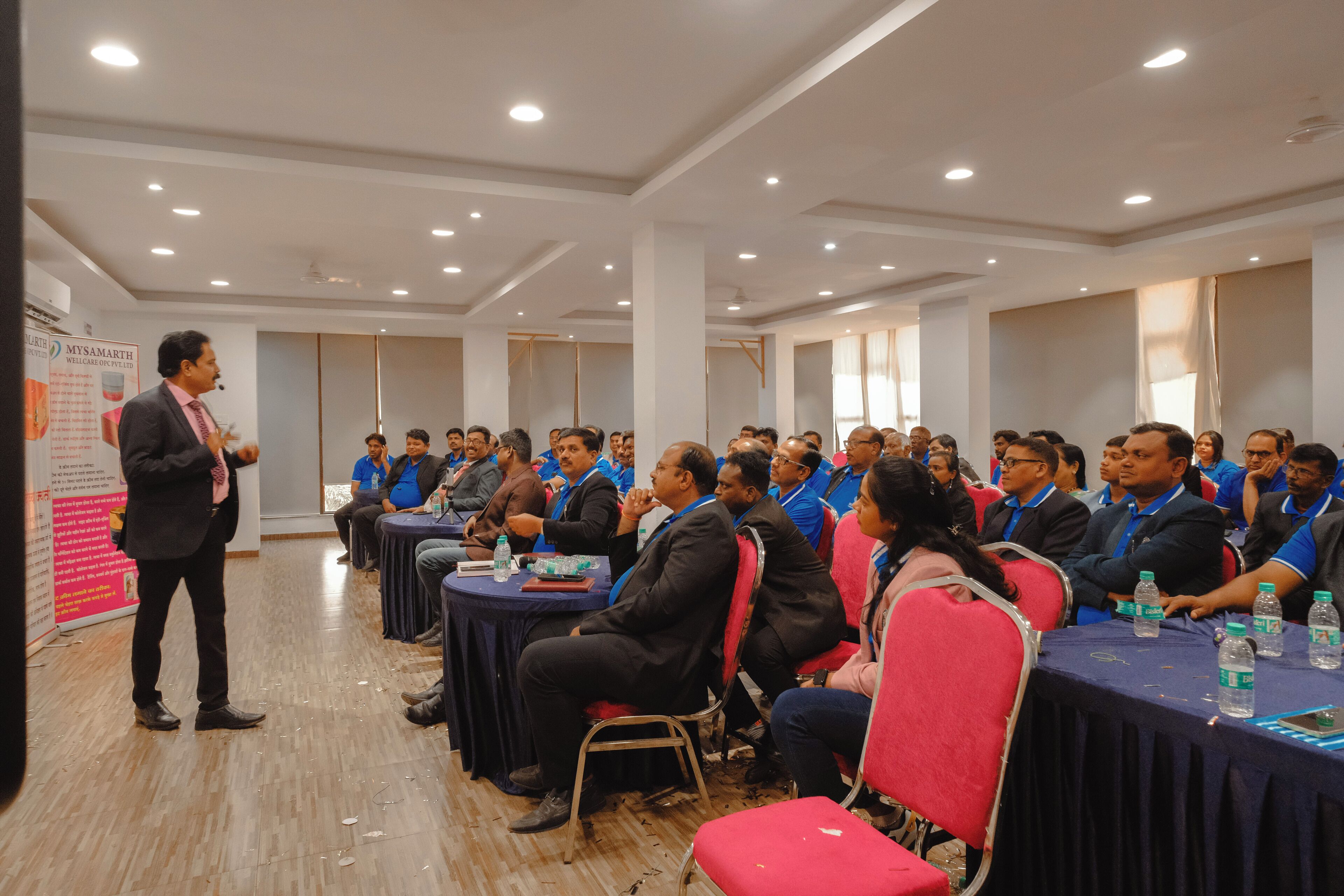 A conference room with round tables, attendees seated, and a speaker at the front.