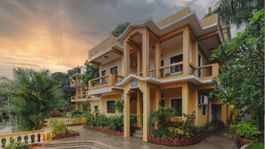 Un hotel de varios pisos con balcones, un jardín con plantas y un sendero, bajo un cielo despejado.
