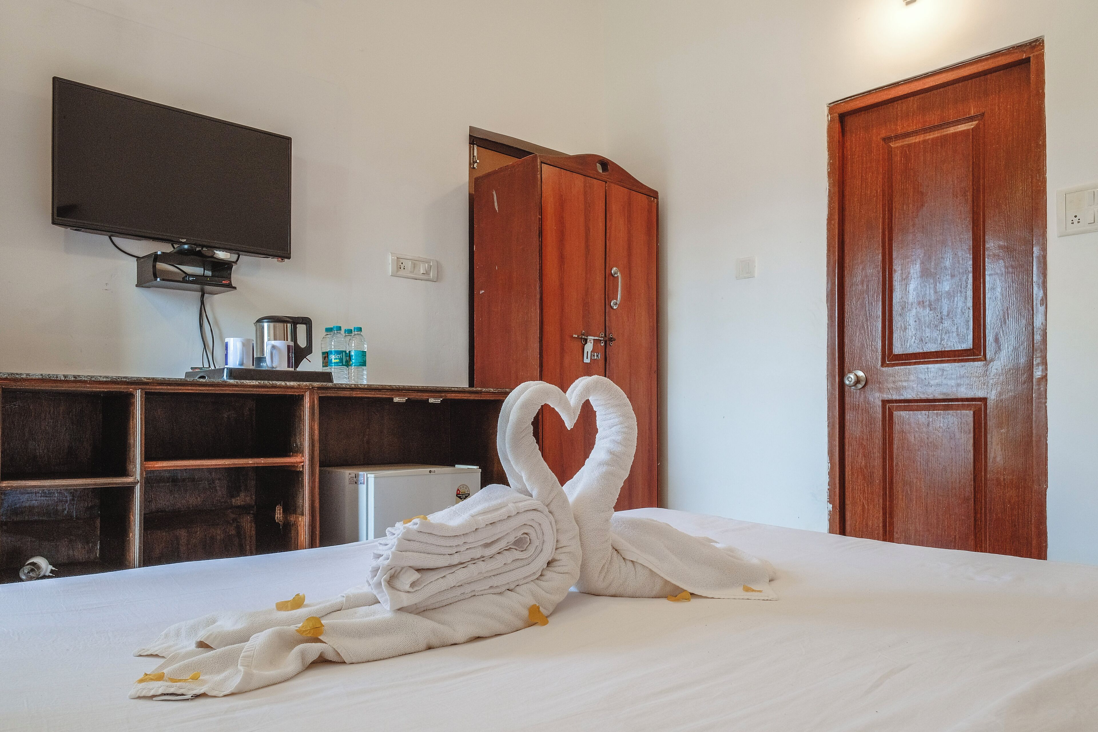 Une chambre d’hôtel avec un lit, un téléviseur fixé au mur, une armoire en bois et une porte en bois.