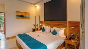 Una habitación de hotel con una cama grande, un cabecero de madera, una mesita de noche con un teléfono y un florero, y un cuadro en la pared.