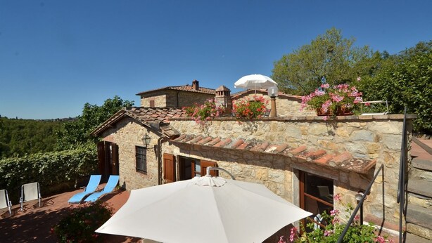 A stone building with a tiled roof, a small dome structure, and a patio area with blue lounge chairs and a white umbrella. - Casuccia di Ama, Gaiole in Chianti, Siena and Chianti (Gaiole in Chianti)