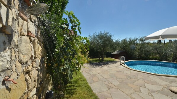 A stone wall with a water feature, a swimming pool, and a covered area with a white umbrella.