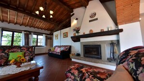 A cozy living room with a fireplace, floral-patterned sofas, and a wooden ceiling. - Casuccia di Ama, Gaiole in Chianti, Siena and Chianti (Gaiole in Chianti)