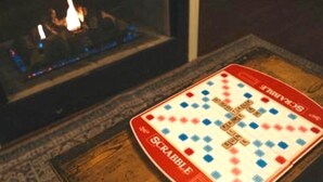 A Scrabble game on a wooden table with a fireplace in the background.
