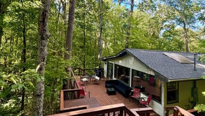 A wooden deck with outdoor furniture, a covered seating area, and a view of a forested area. - HOT TUB, FIRE PIT, DOGS WELCOME, 2 MINUTES to LAKE LURE BEACH and CHIMNEY ROCK (Lake Lure)