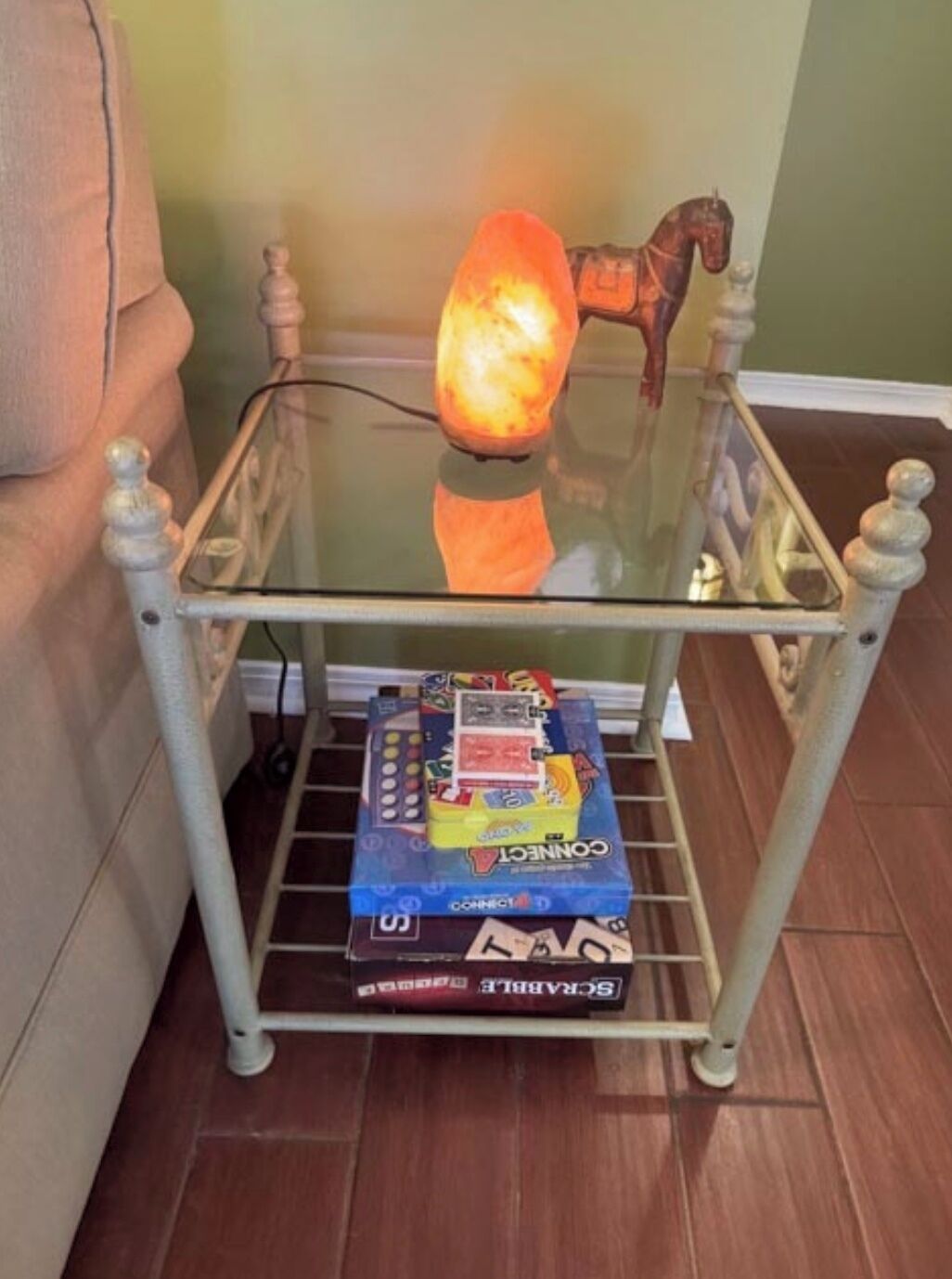 Una mesa con cubierta de vidrio, una lámpara, una figurita de caballo y juegos de mesa.