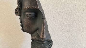 A bust sculpture on a black stand with two small potted plants on either side.