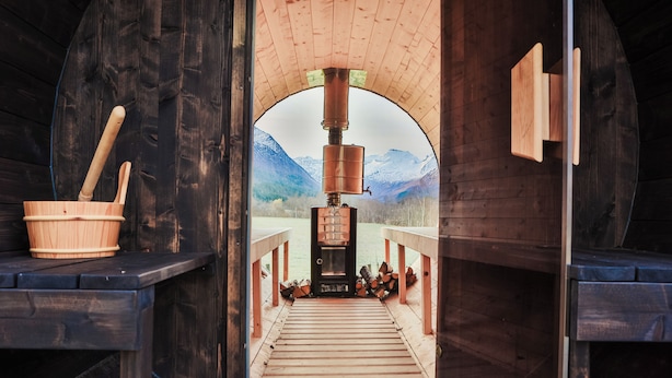 A sauna with a wooden interior, a wooden bench, and a view of mountains through an arched opening.