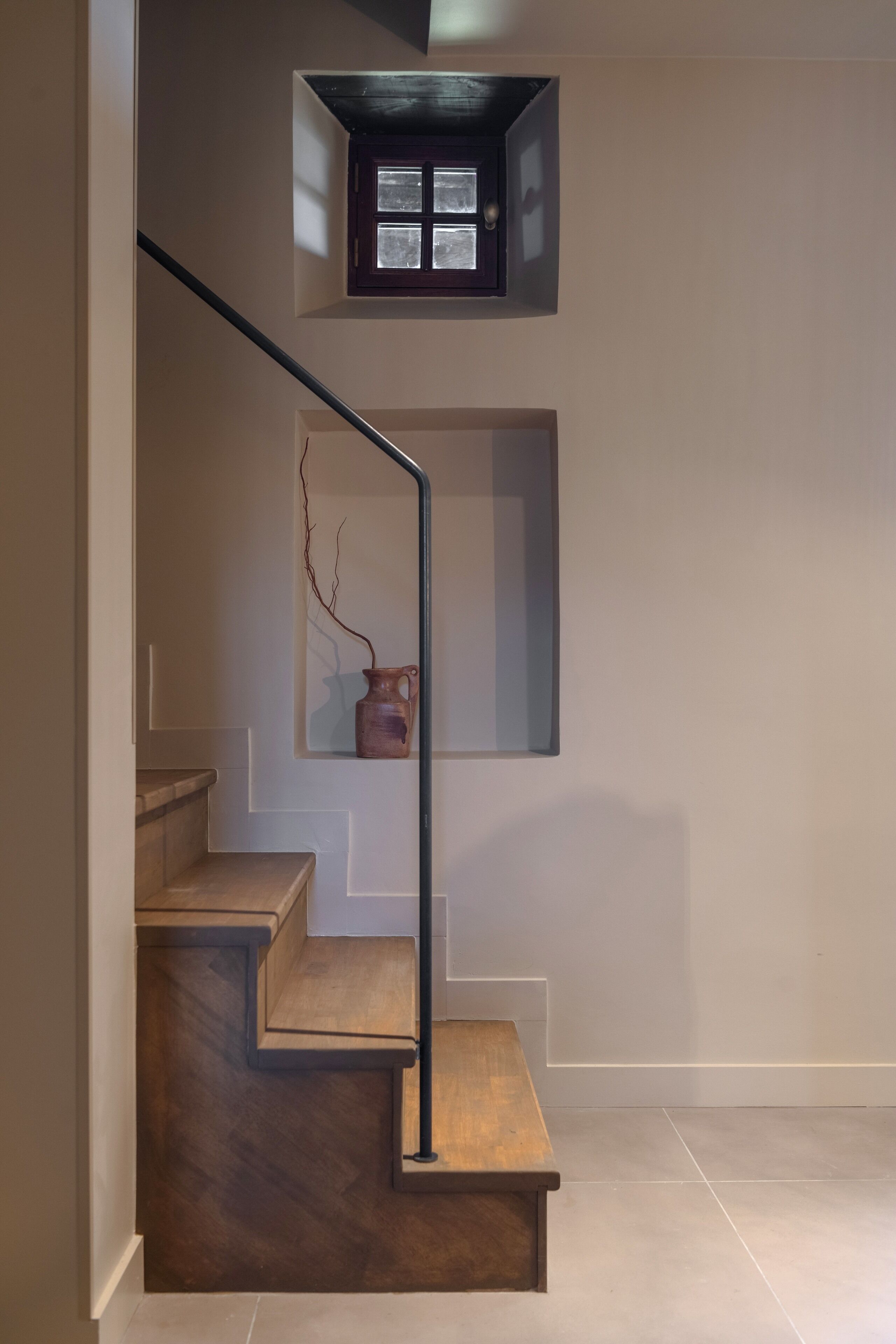 A staircase with wooden steps and a metal handrail, leading to a landing with a small window and a vase.