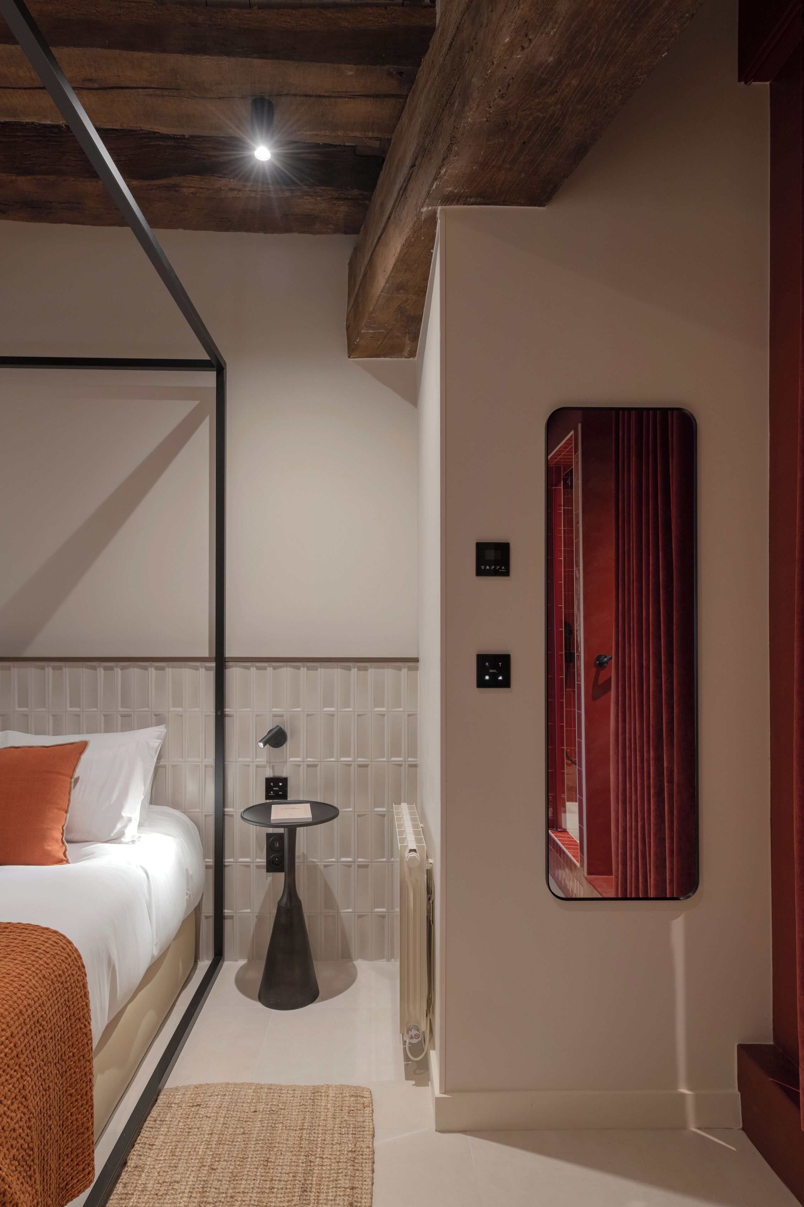 Un dormitorio moderno con una cama, una mesita, un radiador y un espejo en la pared.