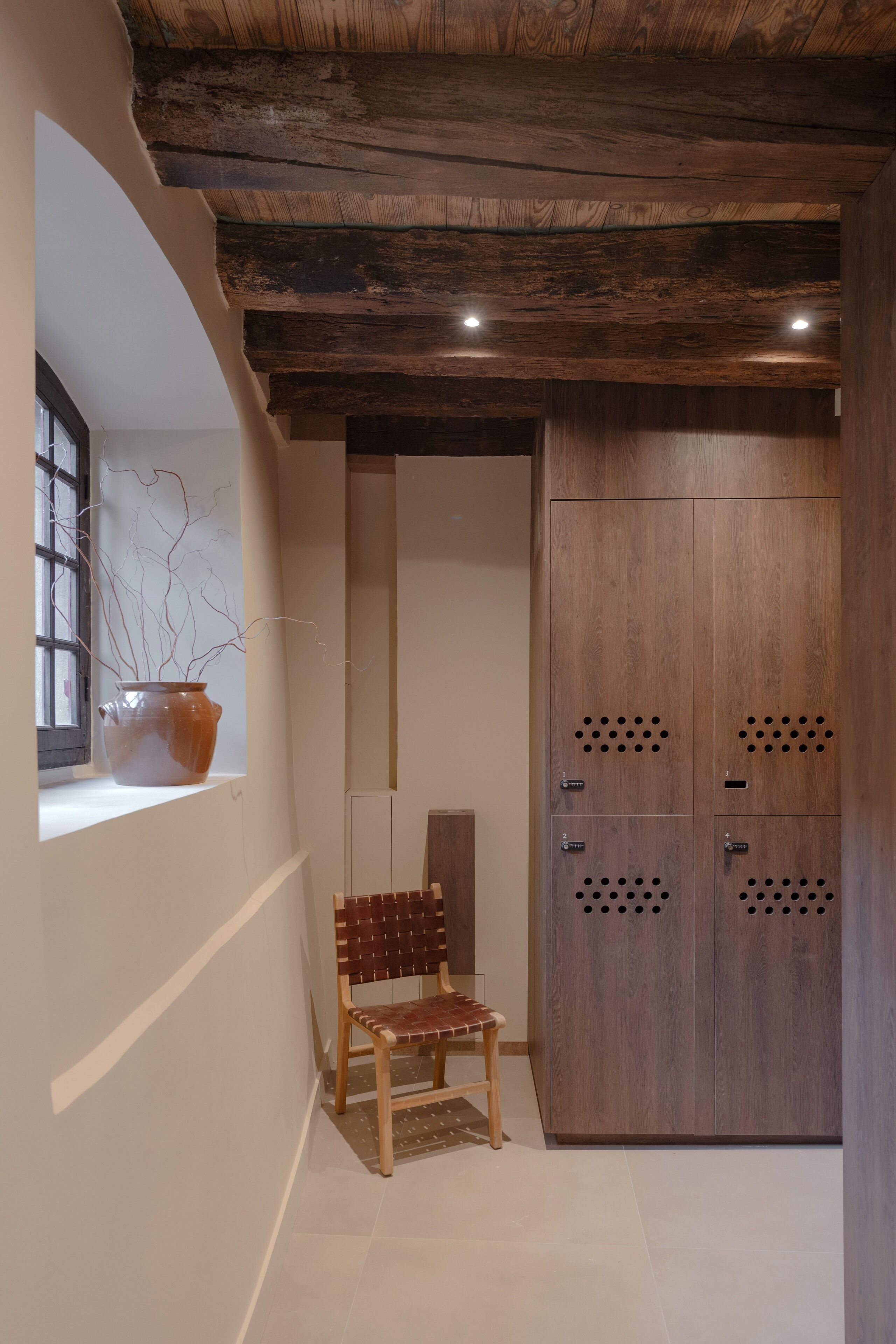 Un couloir avec un banc en bois, une plante en pot et une armoire en bois ornée d’ouvertures circulaires.