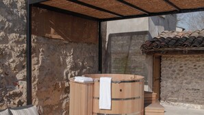 Un espace extérieur aménagé avec un canapé, une table en bois, un jacuzzi et un mur en pierre.