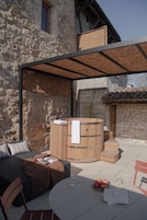 Un espacio exterior con sala de estar, un sofá, una mesa de madera, un jacuzzi y una pared de piedra.