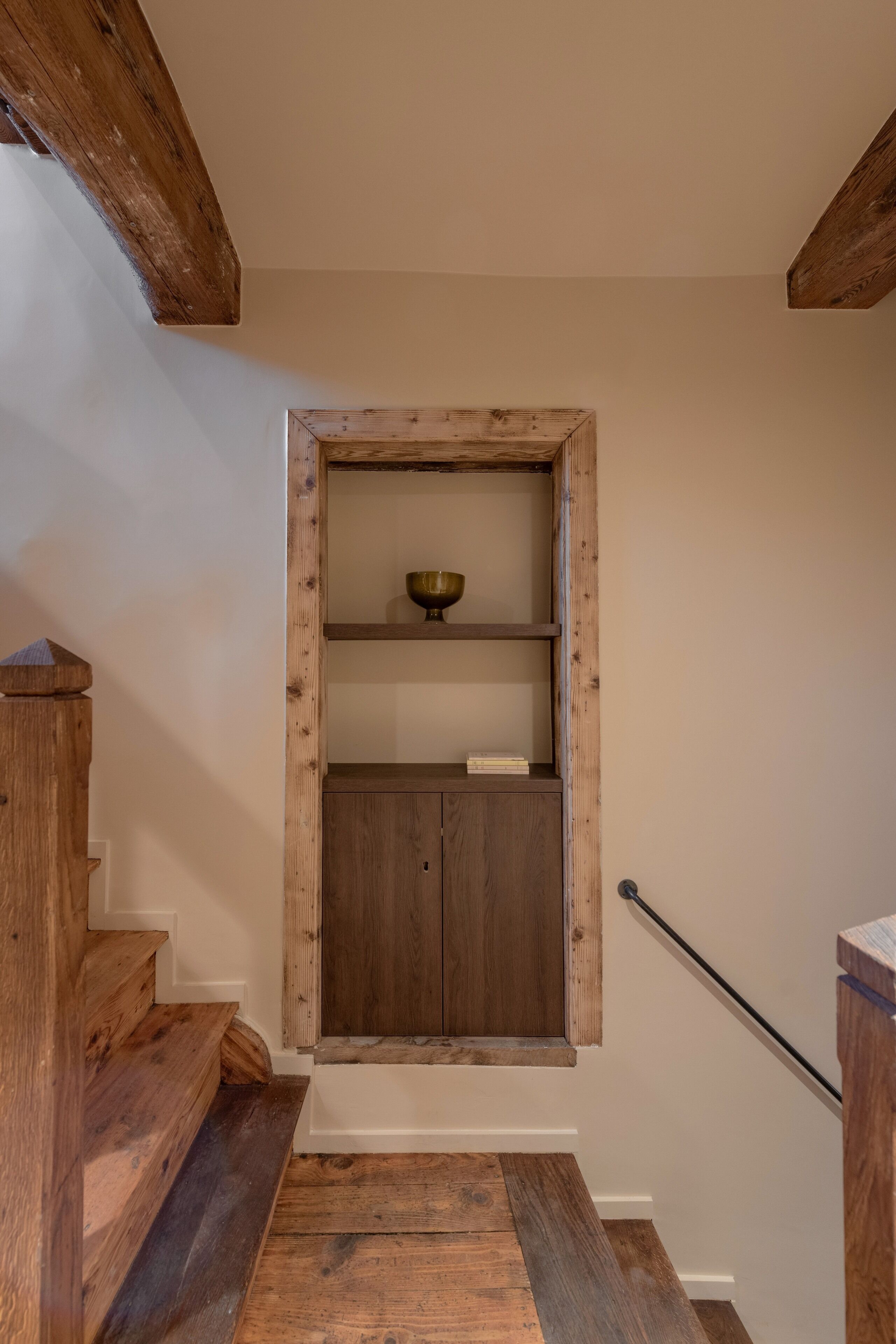 Een houten trap die leidt naar een kamer met een houten deur, een plank met een kom, en een klein kastje.