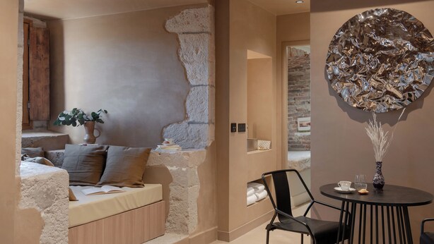 Une pièce chaleureuse avec un mur en pierre, un lit avec des oreillers, une petite table sur laquelle est posé un vase, et une chaise.