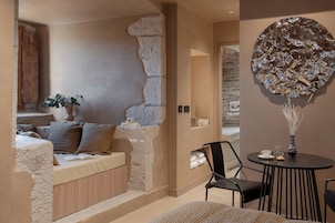 Una habitación acogedora con pared de piedra, una cama con almohadas, una mesita con un jarrón y una silla.
