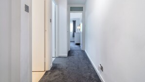 A narrow hallway with white walls and a dark carpet.