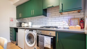 A compact kitchen with green cabinets, a built-in washing machine, a stove, and a tea box.