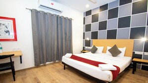 A hotel room with a bed, a desk, a chair, a nightstand, and a wall-mounted air conditioner. - Moonlight Inn (Bengaluru)