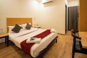 A hotel room with a wooden headboard, a bed with white linens and a red blanket, a bedside table with a remote control, and a wooden floor. - Moonlight Inn (Bengaluru)
