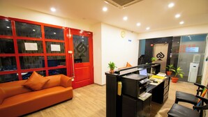 A reception desk with a computer, a black chair, a red door, and a wooden floor. - Moonlight Inn (Bengaluru)
