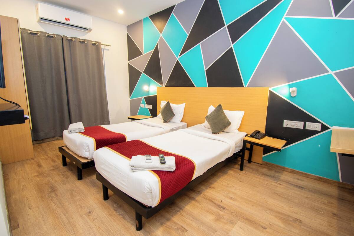 A hotel room with two beds, a desk, a phone, and a wall with geometric patterns.