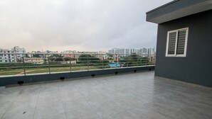 A rooftop terrace with a view of a cityscape, including buildings and a sports field. - Moonlight Inn (Bengaluru)