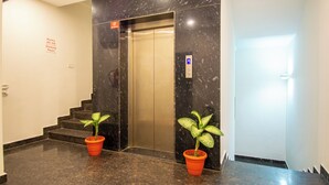 An elevator in a hallway with two potted plants on either side. - Moonlight Inn (Bengaluru)