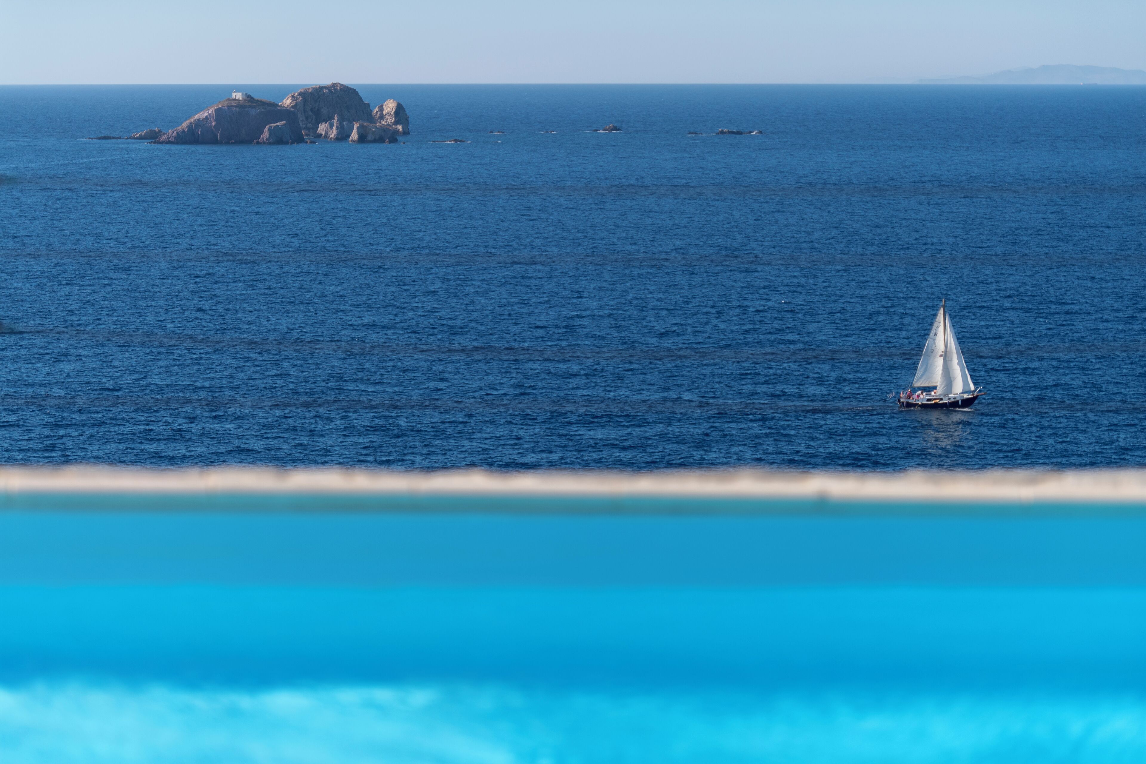 Un velero en un mar tranquilo con una isla rocosa al fondo.