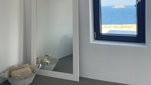 Een slaapkamer met een grote spiegel, een klein raam met uitzicht op zee, en een emmer met een handdoek.