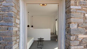 Un couloir étroit aux murs de pierre mène à une pièce où se trouvent un lit et une petite table.