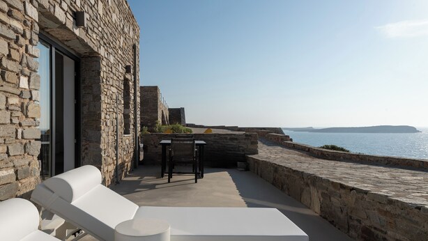 Un bâtiment en pierre doté d’une terrasse avec des chaises longues blanches et une table.