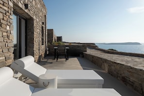 Un edificio de piedra con una terraza que tiene sillones blancos y una mesa.