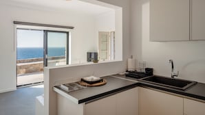 Une cuisine moderne avec un plan de travail noir, un évier et une vue sur la mer grâce à une grande fenêtre.