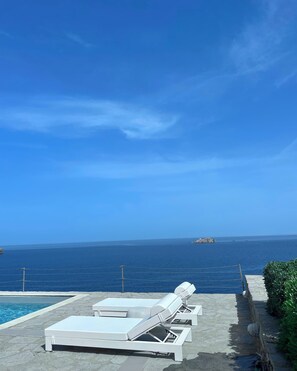 Un espace aménagé au bord de la piscine, avec des chaises longues et une vue sur la mer.