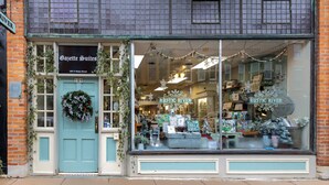 Fachada con un letrero que dice "Gazette Suites" en el número 109 de la calle N Main, que presenta un escaparate grande con varios artículos y un adorno en la puerta.