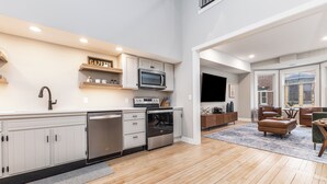 Una cocina moderna con armarios blancos, microondas integrado y lavavajillas. Hay un comedor con mesa y sillas de madera.