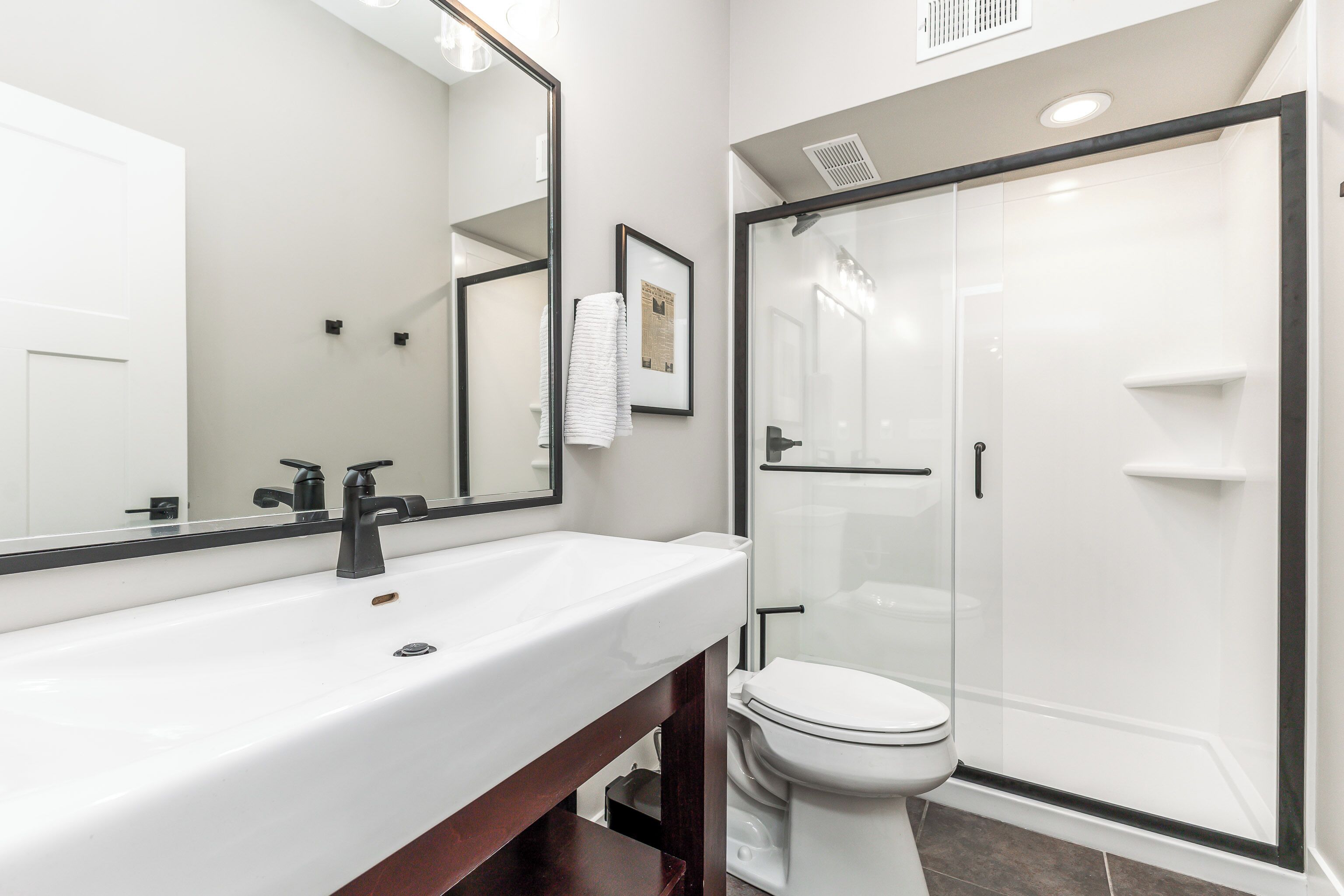 Une salle de bain moderne avec un lavabo blanc, un miroir, des toilettes et une douche à parois de verre.